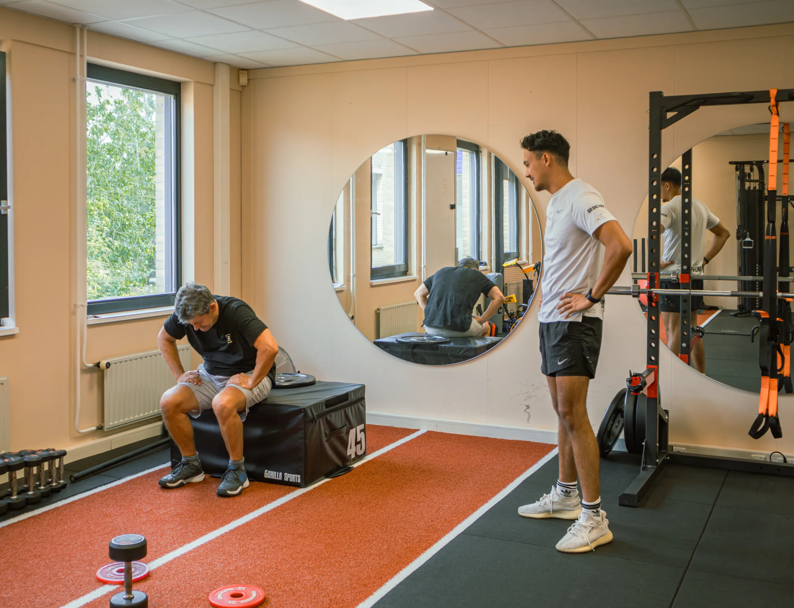 Bryan en een cliënt nemen even pauze in de studio van Bekafit, met de rode sprintbaan en de ronde spiegel