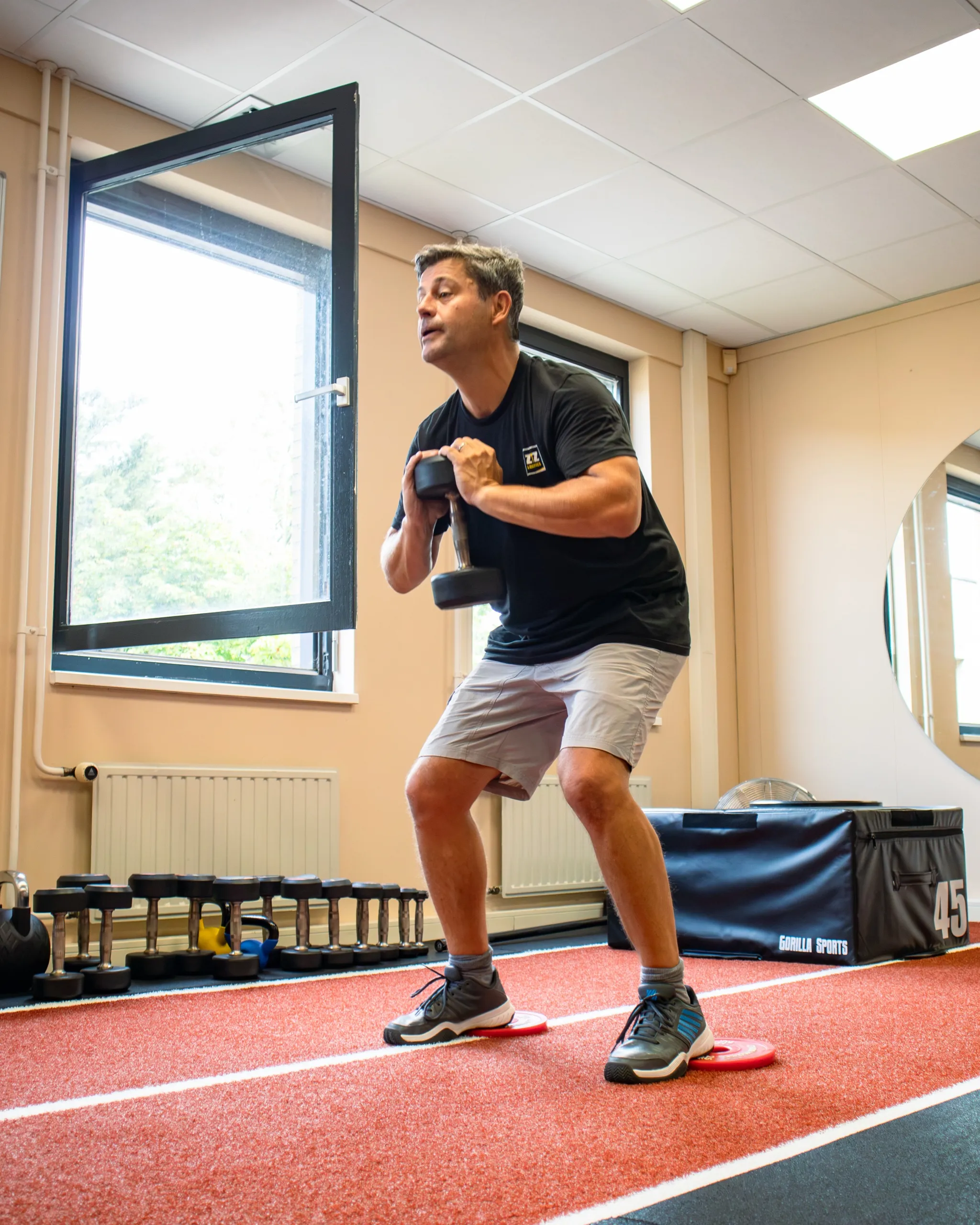 Een cliënt doet een squat met een dumbbell voor de borst bij het open raam van de studio