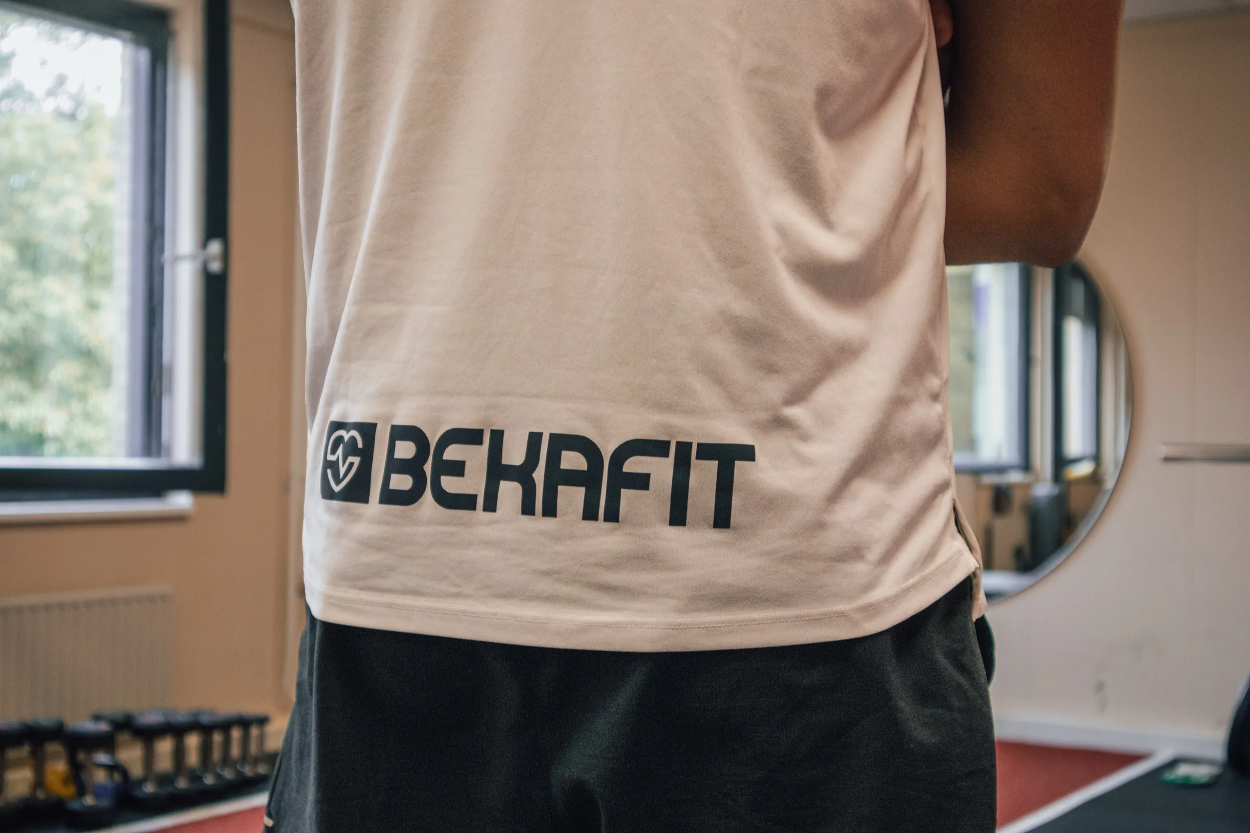 Het Bekafit-logo op het shirt van Bryan, met kettlebells en de ronde spiegel op de achtergrond