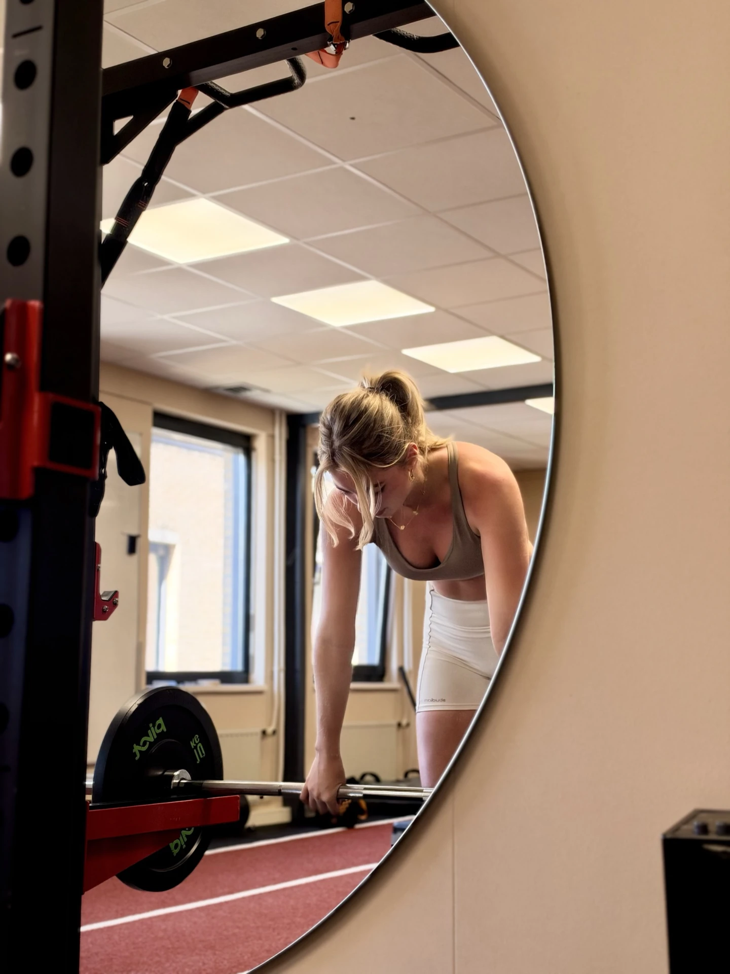 Een sporter pakt de stang van de deadlift op, gezien in de ronde spiegel van de studio van Bekafit